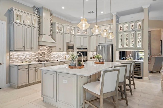 kitchen featuring wine cooler, decorative light fixtures, appliances with stainless steel finishes, an island with sink, and wall chimney exhaust hood