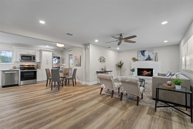 living room with ceiling fan, a fireplace, and light hardwood / wood-style flooring