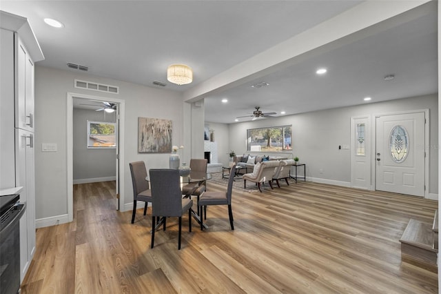 dining area with light wood-type flooring, ceiling fan, and a brick fireplace