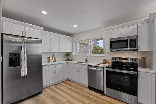 kitchen with light wood-type flooring, stainless steel appliances, white cabinets, and sink