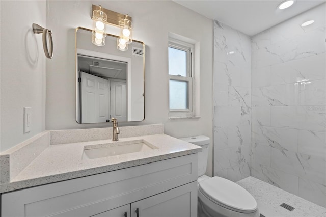 bathroom with toilet, vanity, and a tile shower