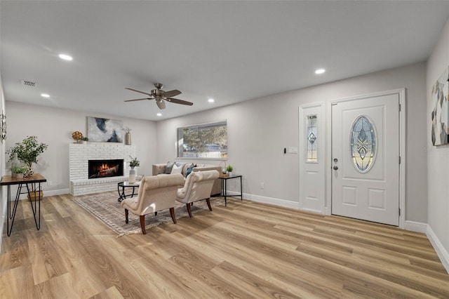 foyer featuring light wood-type flooring, ceiling fan, and a brick fireplace