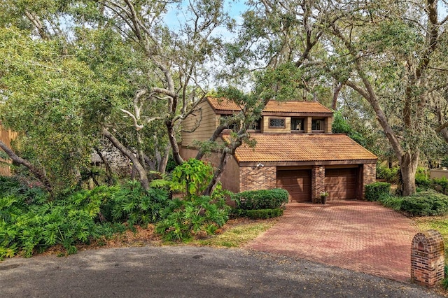 view of front of house with a garage, brick siding, decorative driveway, and a tiled roof