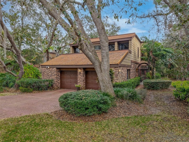 view of front of house featuring decorative driveway, a tile roof, brick siding, an attached garage, and stone siding