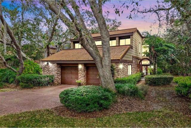 view of front facade featuring an attached garage, brick siding, decorative driveway, and a tiled roof