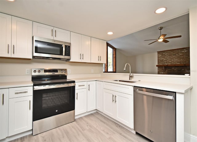 kitchen with kitchen peninsula, sink, white cabinetry, light wood-type flooring, and appliances with stainless steel finishes