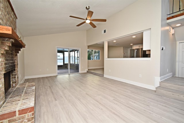 unfurnished living room featuring ceiling fan, high vaulted ceiling, a brick fireplace, and light hardwood / wood-style flooring