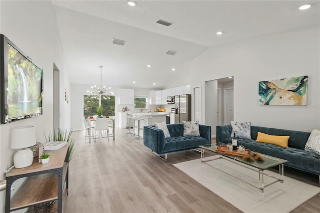 living room with vaulted ceiling, a chandelier, a textured ceiling, and light hardwood / wood-style floors