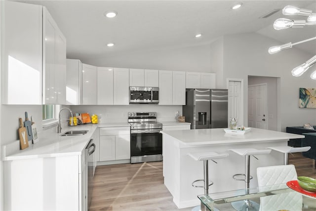 kitchen featuring appliances with stainless steel finishes, a kitchen island, white cabinetry, sink, and a breakfast bar area