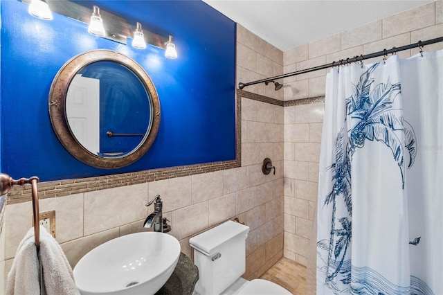 bathroom with sink, curtained shower, toilet, and tile walls