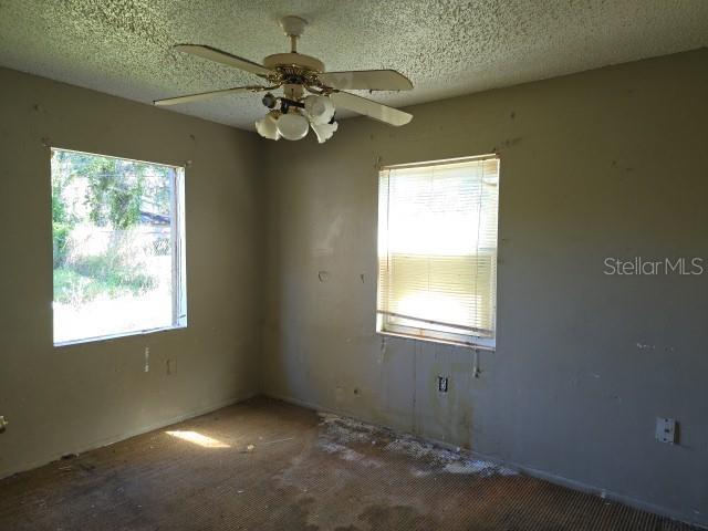 empty room with ceiling fan, a textured ceiling, and a healthy amount of sunlight