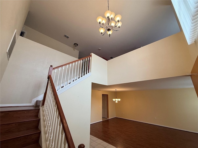 stairway with wood-type flooring, a chandelier, and a high ceiling