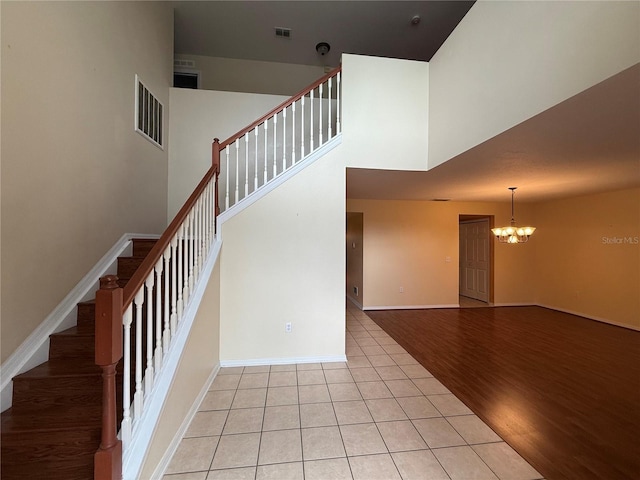 stairs with a towering ceiling, tile patterned flooring, and a notable chandelier