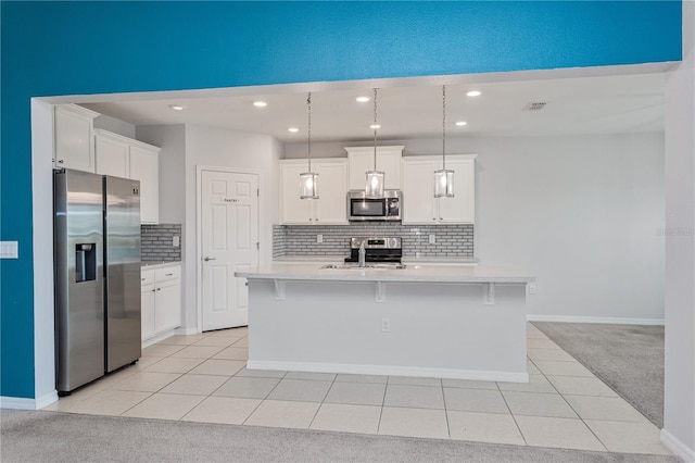 kitchen featuring white cabinetry, light carpet, hanging light fixtures, stainless steel appliances, and a kitchen island with sink