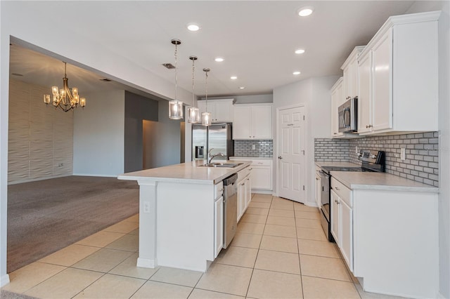 kitchen with appliances with stainless steel finishes, a kitchen island with sink, hanging light fixtures, white cabinets, and light carpet