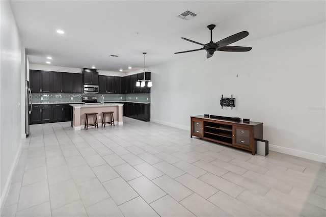 interior space with decorative light fixtures, stainless steel appliances, an island with sink, a kitchen breakfast bar, and ceiling fan