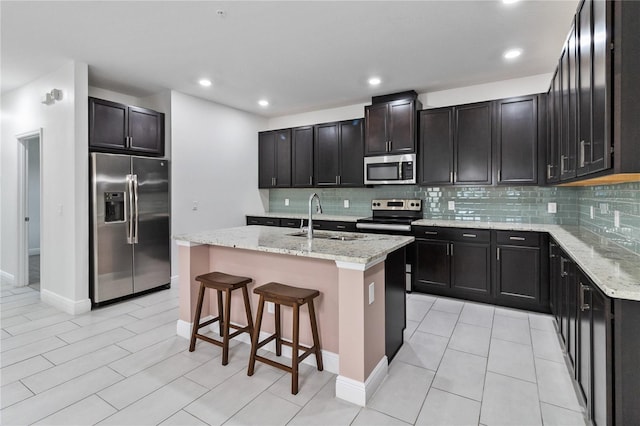 kitchen featuring a center island with sink, appliances with stainless steel finishes, a kitchen breakfast bar, light stone counters, and sink