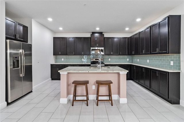 kitchen featuring light stone countertops, stainless steel appliances, an island with sink, a breakfast bar, and light tile patterned floors