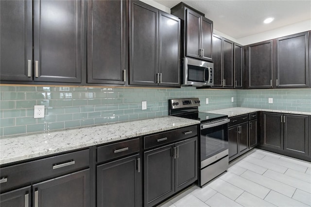 kitchen with light stone countertops, light tile patterned floors, backsplash, and appliances with stainless steel finishes