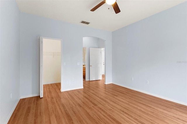 unfurnished bedroom with ceiling fan, a walk in closet, a closet, and light hardwood / wood-style floors