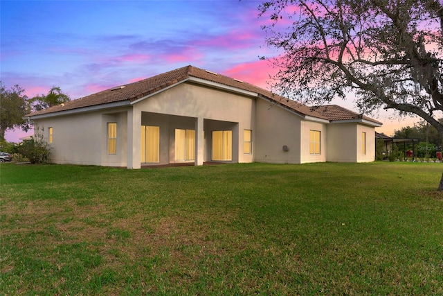 back house at dusk featuring a lawn