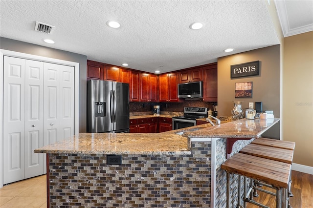 kitchen with kitchen peninsula, stainless steel appliances, a kitchen breakfast bar, crown molding, and light stone counters