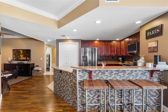 kitchen featuring kitchen peninsula, ornamental molding, stainless steel appliances, and a breakfast bar area