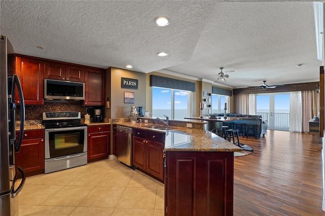 kitchen featuring kitchen peninsula, sink, light stone countertops, stainless steel appliances, and ornamental molding