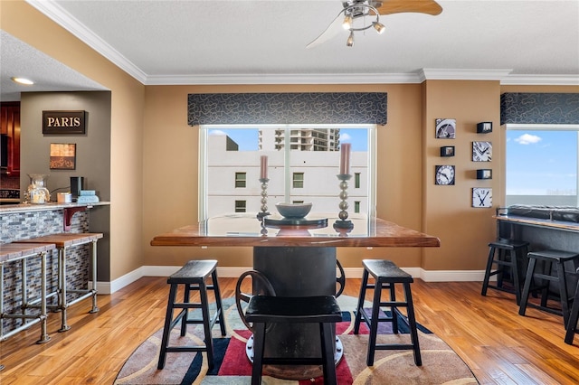 dining area with ceiling fan, light wood-type flooring, bar area, and crown molding