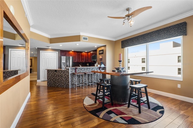 dining room with ceiling fan, a textured ceiling, dark hardwood / wood-style floors, and ornamental molding