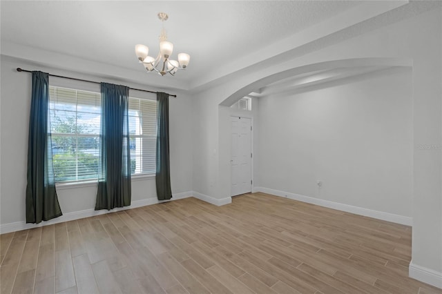 spare room featuring an inviting chandelier and light hardwood / wood-style flooring