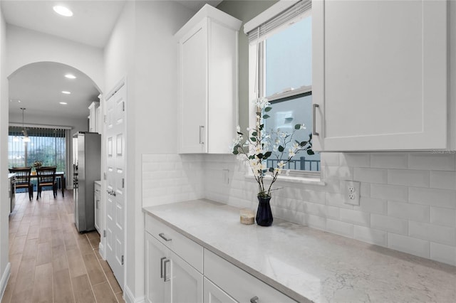 kitchen featuring stainless steel fridge, white cabinetry, hanging light fixtures, light stone counters, and tasteful backsplash