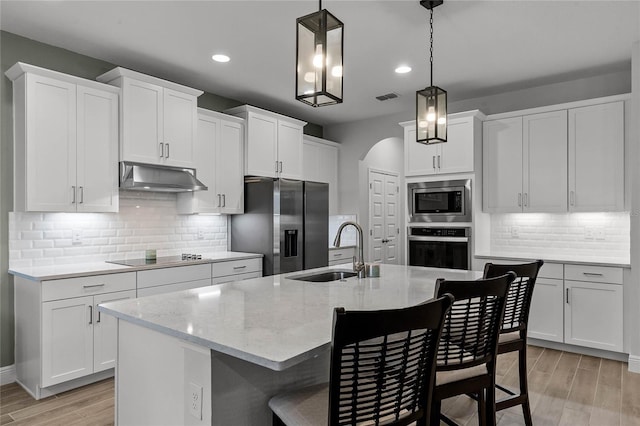 kitchen featuring sink, appliances with stainless steel finishes, white cabinetry, hanging light fixtures, and a center island with sink