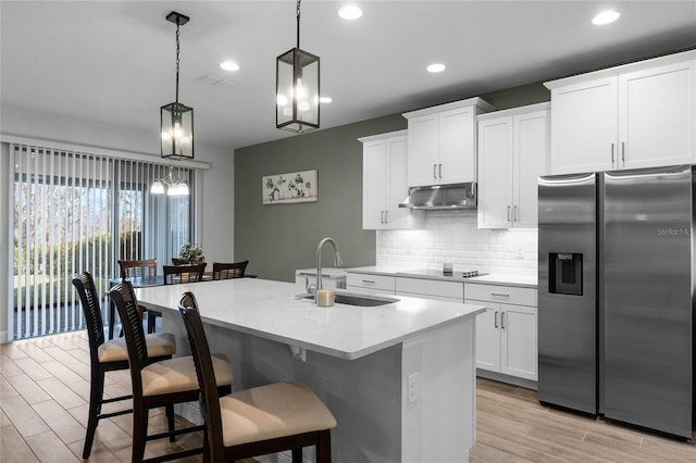 kitchen featuring pendant lighting, white cabinetry, backsplash, stainless steel refrigerator with ice dispenser, and an island with sink