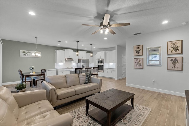 living room featuring ceiling fan with notable chandelier and light hardwood / wood-style flooring