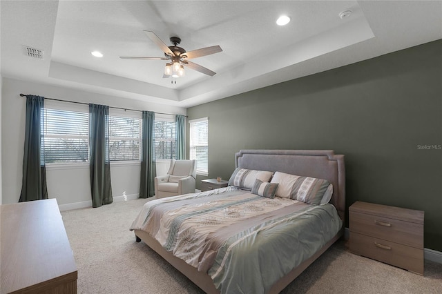 carpeted bedroom with ceiling fan and a tray ceiling