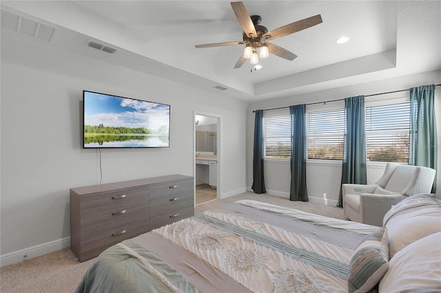 bedroom featuring ceiling fan, ensuite bathroom, a raised ceiling, and light carpet