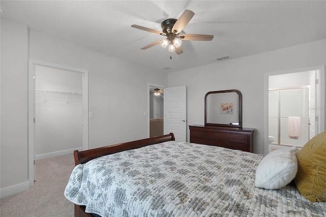 carpeted bedroom featuring ensuite bath, a walk in closet, a closet, and ceiling fan