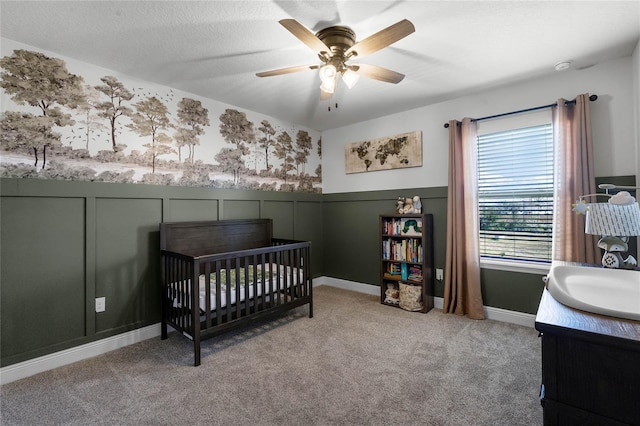 carpeted bedroom featuring ceiling fan, a nursery area, sink, and a textured ceiling