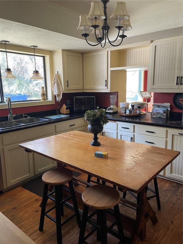 kitchen with a notable chandelier, dark hardwood / wood-style floors, sink, a kitchen breakfast bar, and cream cabinets