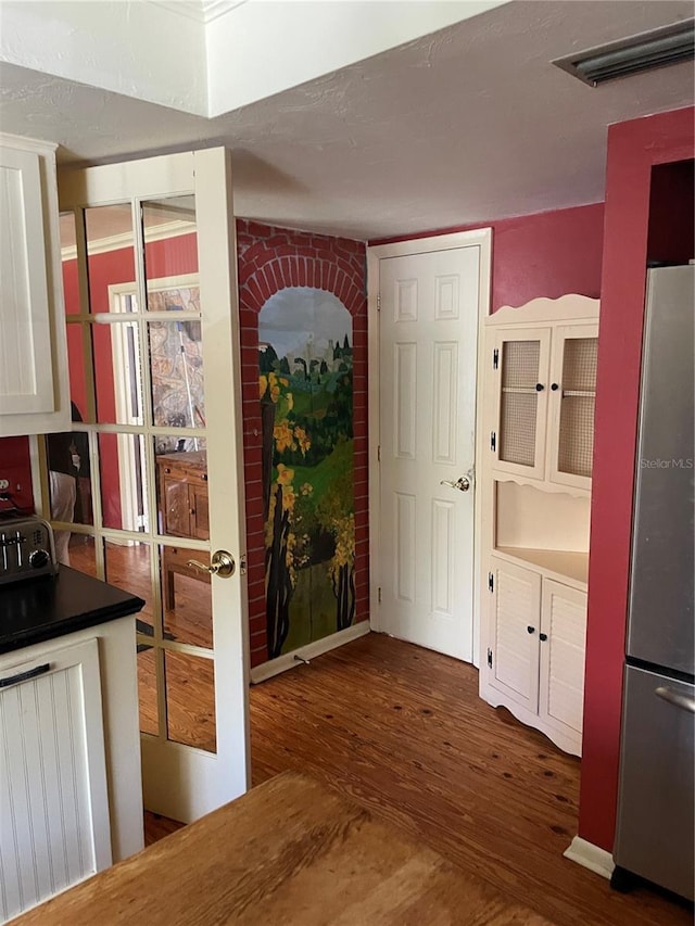 kitchen featuring white cabinetry, stainless steel fridge, dark hardwood / wood-style floors, brick wall, and radiator heating unit