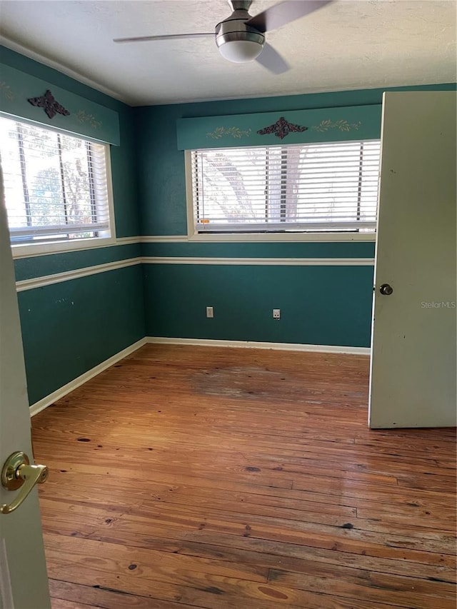 spare room with ceiling fan, plenty of natural light, and wood-type flooring