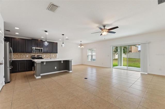 kitchen featuring appliances with stainless steel finishes, a center island with sink, hanging light fixtures, a breakfast bar area, and sink