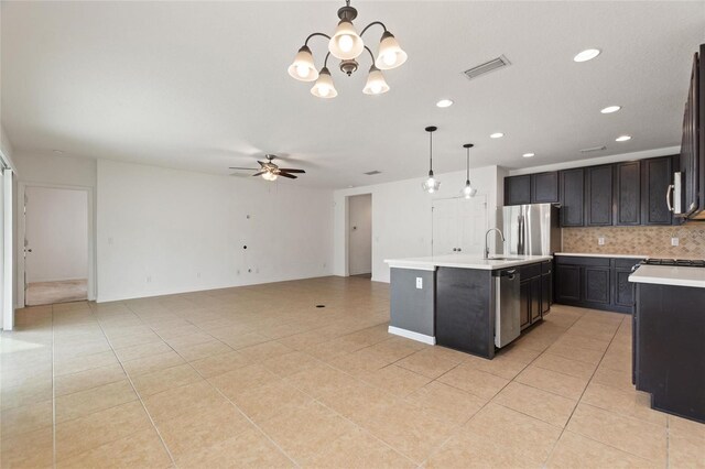 kitchen with a kitchen island with sink, stainless steel appliances, hanging light fixtures, light tile patterned floors, and ceiling fan with notable chandelier