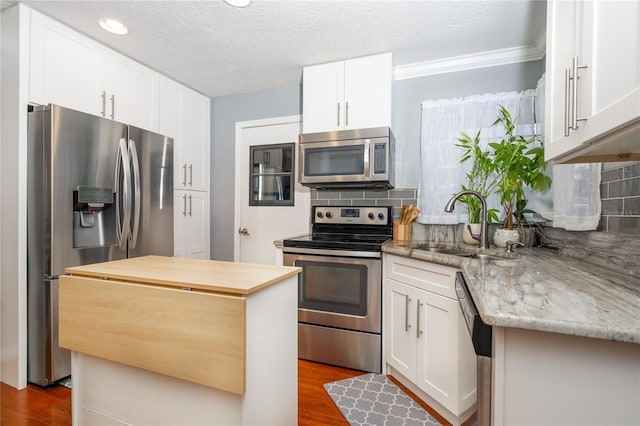 kitchen featuring sink, backsplash, stainless steel appliances, light stone countertops, and white cabinets