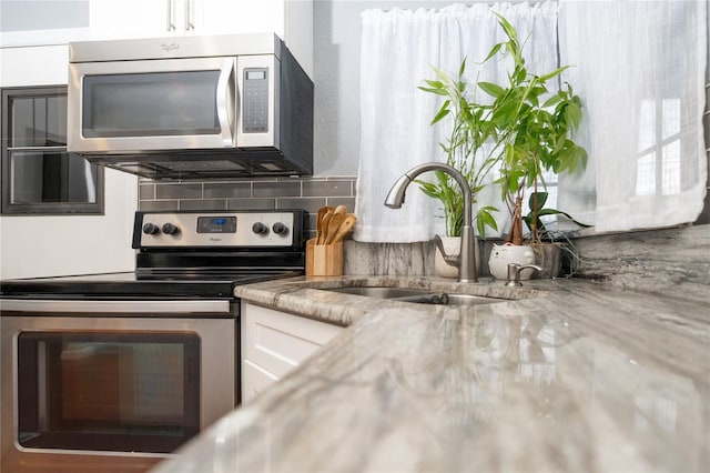 kitchen featuring stainless steel appliances, white cabinetry, sink, and backsplash