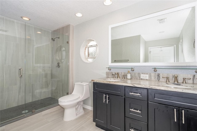 bathroom featuring a shower with door, vanity, a textured ceiling, and toilet