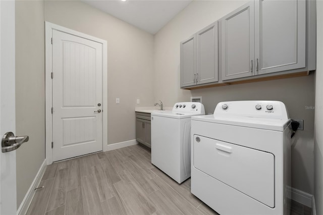 laundry area with cabinet space, baseboards, light wood-type flooring, separate washer and dryer, and a sink