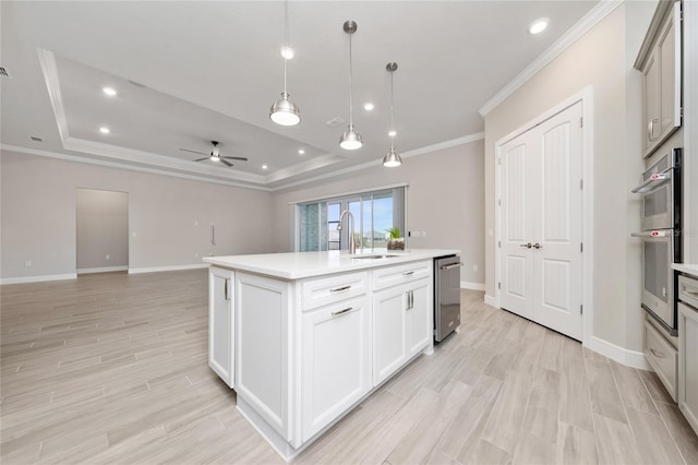 kitchen featuring a tray ceiling, light countertops, hanging light fixtures, appliances with stainless steel finishes, and a kitchen island with sink