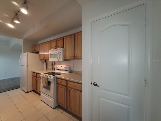 kitchen with track lighting, light countertops, brown cabinets, light tile patterned flooring, and white appliances